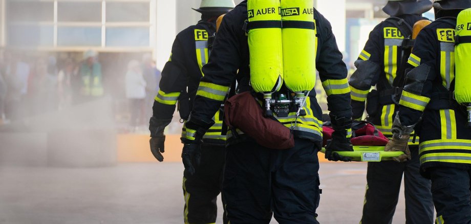 Hier sehen Sie vier Feuerwehrleute die eine Krankentrage tragen.